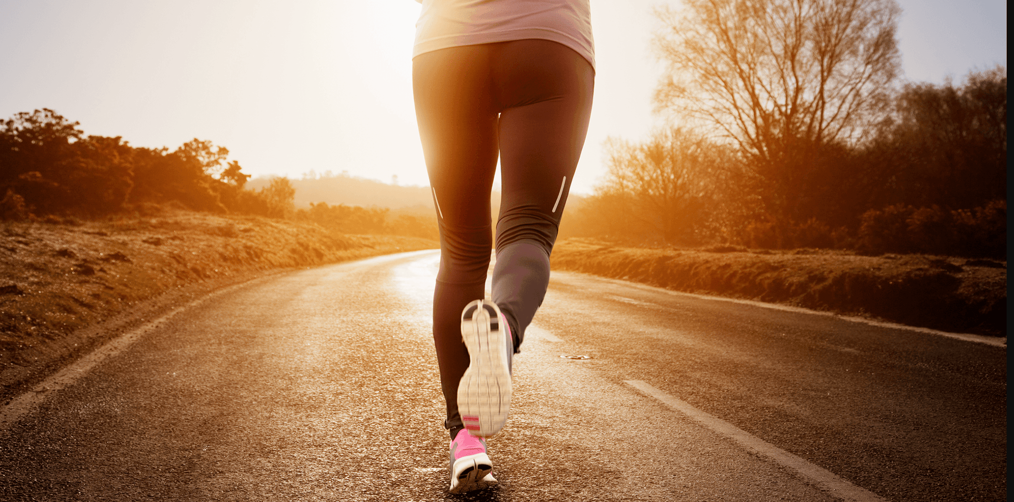 woman's legs running in the sunrise on a road 